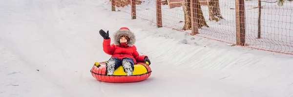 雪のチューブで楽しんでいる子供。男の子はチューブに乗っている。子供のための冬の楽しみ｜バナー、ロングフォーマット — ストック写真