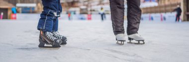 Genç bir anne, oğluna buz pateni pistinde buz pateni öğretiyor. Aile, kış tatilini açık havada, Banner, Long Format 'ta geçiriyor.