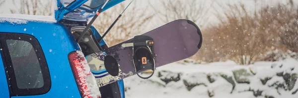 The snowboard does not fit into the car. A snowboarder is trying to stick a snowboard into a car. Humor, fun BANNER, LONG FORMAT — Stock Photo, Image