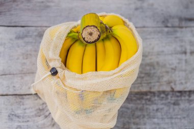 Banana in a reusable bag on a stylish wooden kitchen surface. Zero waste concept, plastic free concept. Healthy clean eating diet and detox. Summer fruits