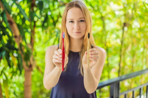 Woman holds eco natural bamboo toothbrush and in other hand plastic toothbrush. rustic background. sustainable lifestyle concept. zero waste. choice plastic free items
