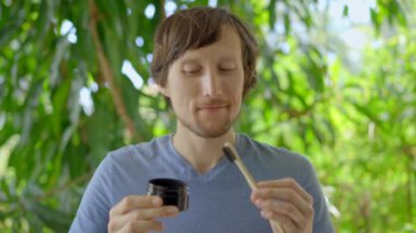 A young man in a green environment brushes his teeth with a black active charcoal powder for teeth whitening. He uses a toothbrush made of a bamboo. Concept of eco friendly zero waste bamboo products