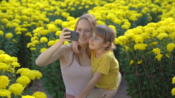 Młoda kobieta i jej syn robią selfie stojąc pośród wielu żółtych kwiatów, które ludzie z Azji Wschodniej wyrastają, by świętować nowy rok na Księżycu. Podróż do Azji koncepcja — Wideo stockowe