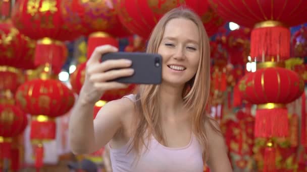 Una joven mujer hace una selfie de pie entre un montón de faroles chinos rojos que la gente de Asia oriental utiliza para celebrar un año nuevo lunar. Viajes a Asia concepto . — Vídeos de Stock