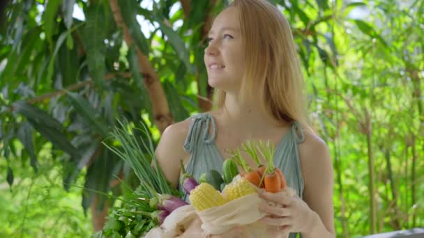 Genç bir kadın tekrar kullanılabilir bir çantaya çeşitli sebzeler koyar. Kirliliği plastikle azaltma kavramı. Azalt ve tekrar kullan — Stok video