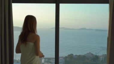 Sahilde ve gündoğumunda panoramik manzaralı bir dairede genç bir kadın. Kablosuz kulaklık takar ve müzik dinler.