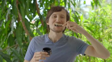A young man in a green environment brushes his teeth with a black active charcoal powder for teeth whitening. He uses a toothbrush made of a bamboo. Concept of eco friendly zero waste bamboo products
