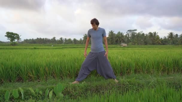 Un joven tiene un entrenamiento de yoga en un hermoso campo de arroz. Viajes a Asia concepto — Vídeo de stock