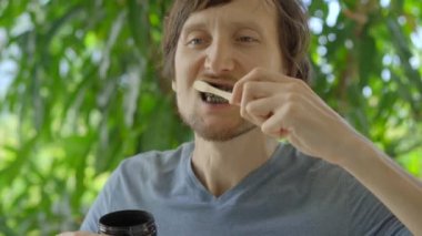 A young man in a green environment brushes his teeth with a black active charcoal powder for teeth whitening. He uses a toothbrush made of a bamboo. Concept of eco friendly zero waste bamboo products