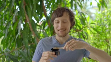 A young man in a green environment brushes his teeth with a black active charcoal powder for teeth whitening. He uses a toothbrush made of a bamboo. Concept of eco friendly zero waste bamboo products