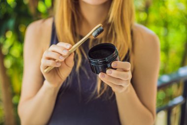 Young woman brush teeth using Activated charcoal powder for brushing and whitening teeth. Bamboo eco brush