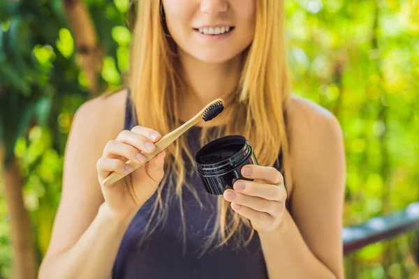 Молодая женщина чистит зубы с помощью активированного угольного порошка для чистки и отбеливания зубов. Эко-кисть бамбука — стоковое фото