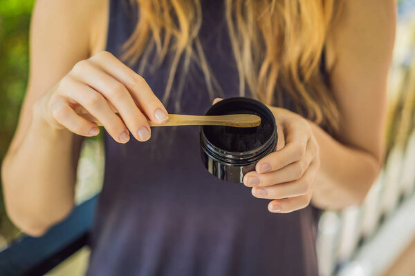 Молодая женщина чистит зубы с помощью активированного угольного порошка для чистки и отбеливания зубов. Эко-кисть бамбука
