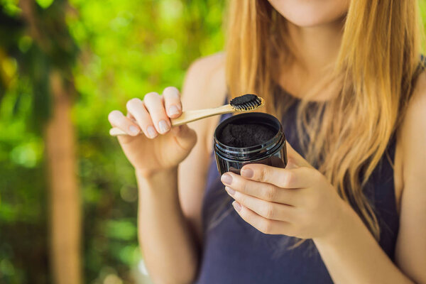 Молодая женщина чистит зубы с помощью активированного угольного порошка для чистки и отбеливания зубов. Эко-кисть бамбука
