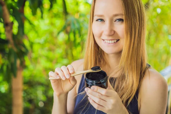 Νεαρή γυναίκα βουρτσίστε τα δόντια χρησιμοποιώντας ενεργοποιημένη σκόνη άνθρακα για το βούρτσισμα και λεύκανση δοντιών. Οικολογικό πινέλο μπαμπού — Φωτογραφία Αρχείου