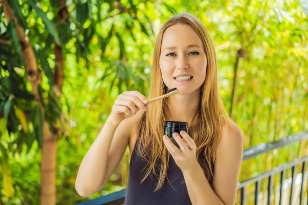 Молодая женщина чистит зубы с помощью активированного угольного порошка для чистки и отбеливания зубов. Эко-кисть бамбука — стоковое фото