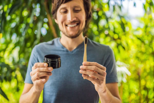 Young man brush teeth using Activated charcoal powder for brushing and whitening teeth. Bamboo eco brush