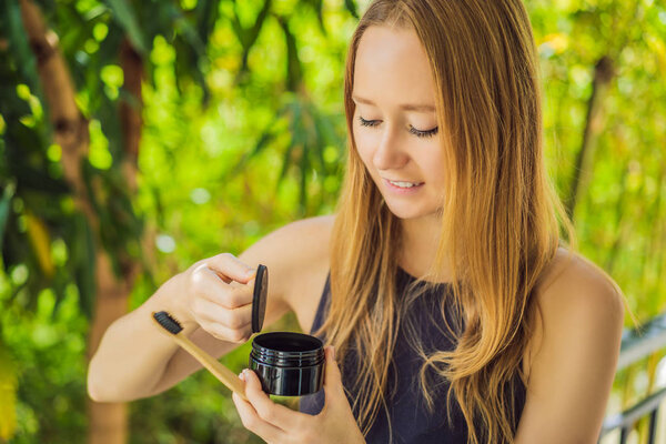 Молодая женщина чистит зубы с помощью активированного угольного порошка для чистки и отбеливания зубов. Эко-кисть бамбука
