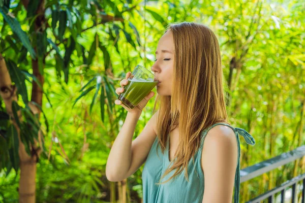 Młoda kobieta pije sok selerowy, zdrowy napój, seler na drewnianym tle — Zdjęcie stockowe