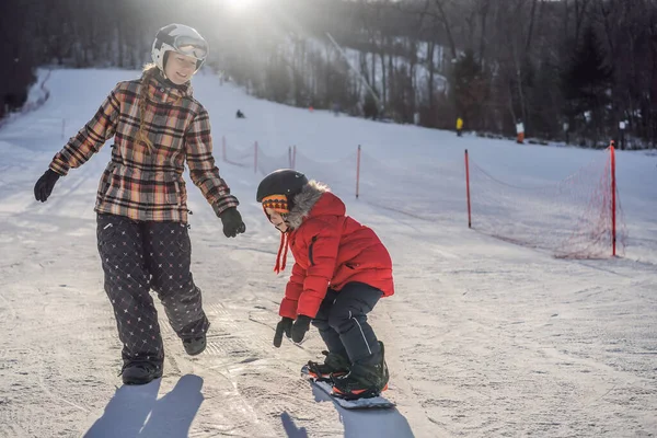 Matka uczy syna snowboardingu. Zajęcia dla dzieci w zimie. Zimowy sport dla dzieci. Styl życia — Zdjęcie stockowe