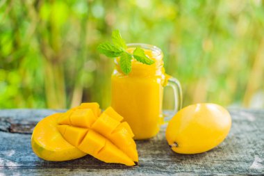 Mango smoothie cam Mason kavanoza ve mango eski ahşap arka plan üzerinde. Mango shake. Tropikal meyve kavramı