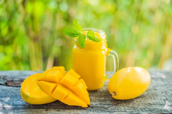 Frullato di mango in un barattolo di vetro Mason e mango sul vecchio sfondo di legno. Scuotere il mango. Concetto di frutta tropicale — Foto Stock