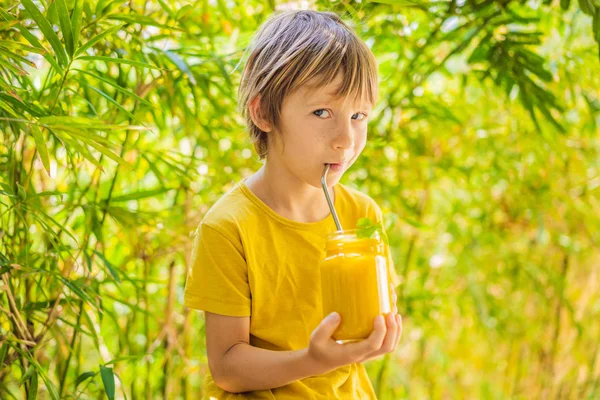 Boy drinking juicy smoothie from mango in glass mason jar. Healthy life concept, copy space