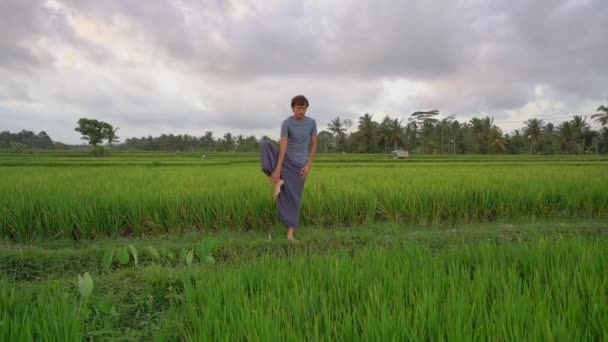 Un joven tiene un entrenamiento de yoga en un hermoso campo de arroz. Viajar a Asia concepto. Vídeo en cámara lenta — Vídeo de stock