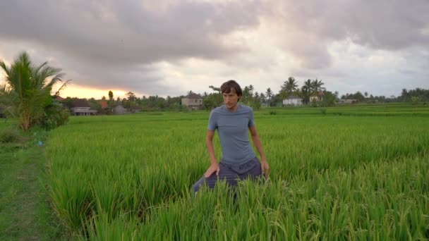 Un joven tiene un entrenamiento de yoga en un hermoso campo de arroz. Viajar a Asia concepto. Vídeo en cámara lenta — Vídeo de stock