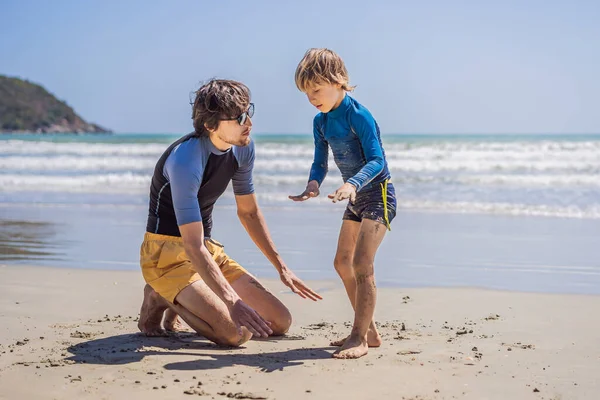 Padre o istruttore che insegna al figlio a navigare in mare in vacanza o in vacanza. Viaggio e sport con bambini concetto. Lezione di surf per bambini — Foto Stock