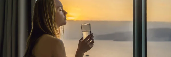 Жінка п'є воду вранці на фоні вікна з видом на море BANNER, LONG FORMAT — стокове фото