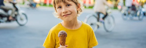 Симпатичный маленький мальчик, ест большое мороженое в парке, улыбается в камеру, летнее время баннер, длинный Формат — стоковое фото
