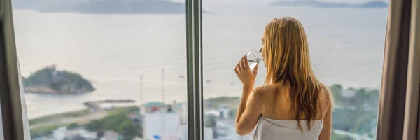 Woman drinks water in the morning on a background of a window with a sea view BANNER, LONG FORMAT — Stock Photo, Image