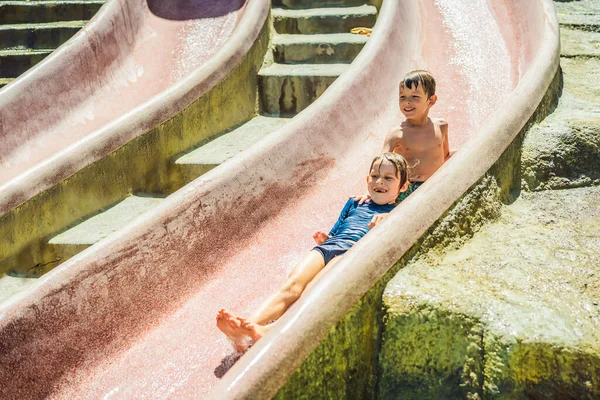Los niños montan en un tobogán en un parque acuático. Feliz infancia. — Foto de Stock