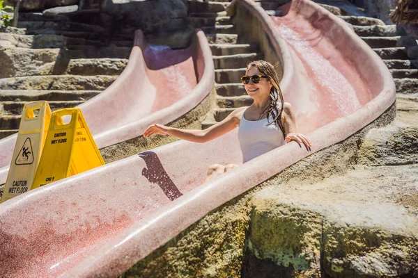 Žena na kamenné vodní skluzavce v aquaparku. Aqua park, Girl slide down on water slide — Stock fotografie