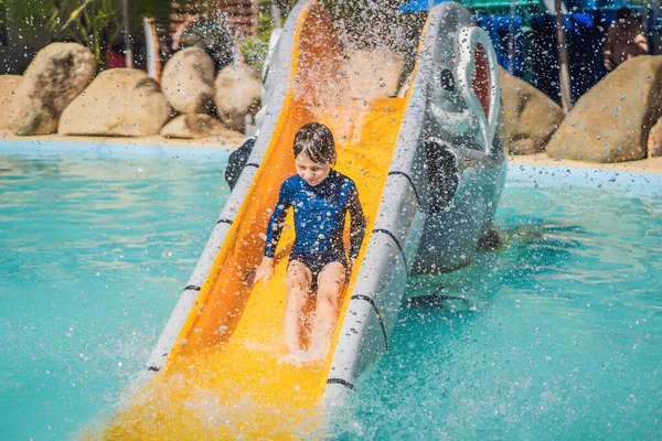 Sonriente joven cabalgando por un tobogán de agua amarillo — Foto de Stock