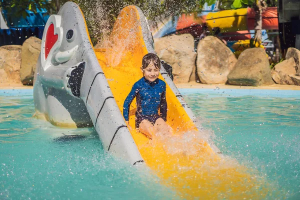 Smiling Young boy riding down a yellow water slide — Stock Photo, Image