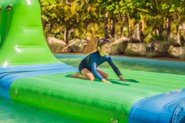 Yakışıklı çocuk havuzda şişme engelli koşusu yapıyor.