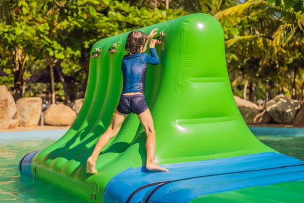 Lindo chico corre una carrera de obstáculos inflable en la piscina — Foto de Stock