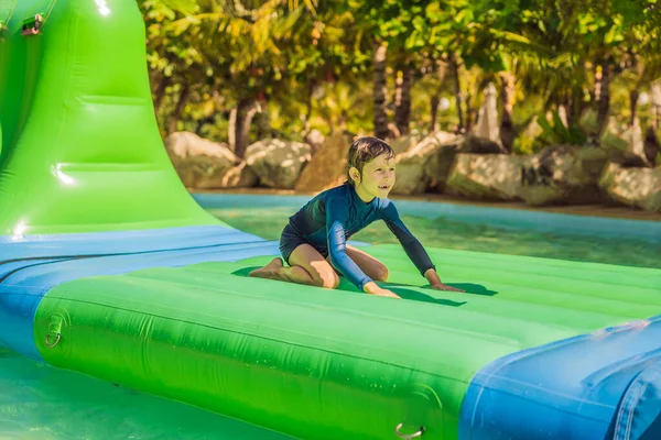 Söt pojke kör en uppblåsbar hinderbana i poolen — Stockfoto