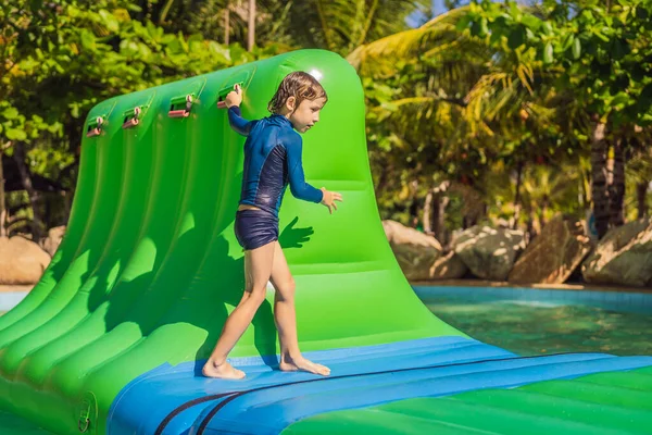 Anak laki-laki lucu menjalankan sebuah rintangan inflatable di kolam renang — Stok Foto