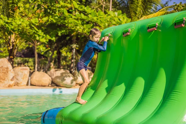 Lindo chico corre una carrera de obstáculos inflable en la piscina —  Fotos de Stock