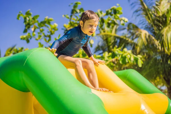 Rapaz bonito corre um curso de obstáculo inflável na piscina — Fotografia de Stock