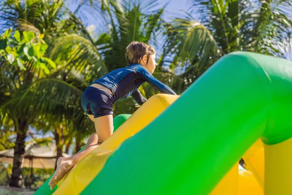 Rapaz bonito corre um curso de obstáculo inflável na piscina — Fotografia de Stock