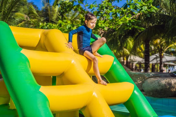 Lindo chico corre una carrera de obstáculos inflable en la piscina — Foto de Stock