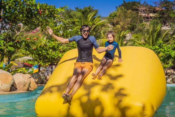 Papá e hijo pasan por una carrera de obstáculos inflable en la piscina — Foto de Stock