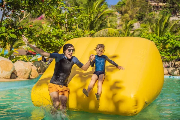 Papá e hijo pasan por una carrera de obstáculos inflable en la piscina — Foto de Stock