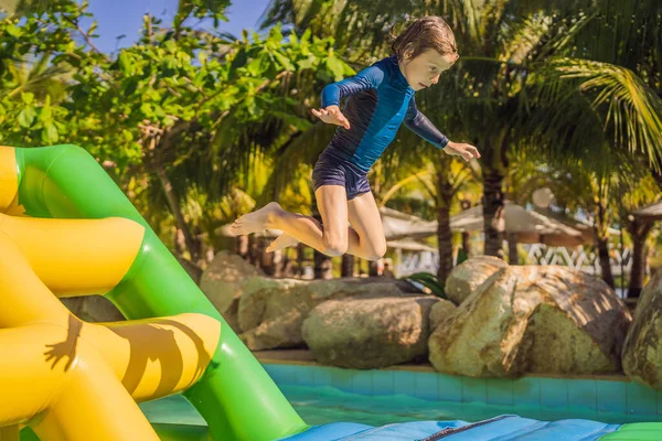 Lindo chico corre una carrera de obstáculos inflable en la piscina — Foto de Stock