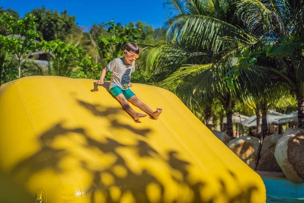 Lindo chico corre una carrera de obstáculos inflable en la piscina — Foto de Stock