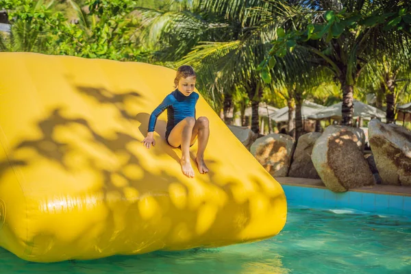 Netter Junge läuft einen aufblasbaren Hindernisparcour im Pool — Stockfoto